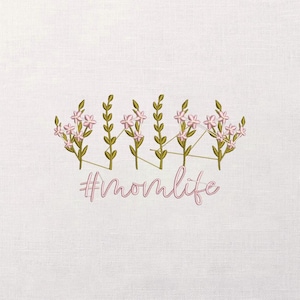May include: Embroidered design on white fabric featuring pink flowers and green stems. The text "#momlife" is stitched in a cursive font below the floral arrangement. The design is centered on the fabric.