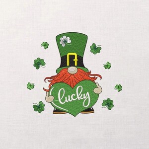 Peut inclure: Broderie d'un gnome de la Saint-Patrick tenant un cœur vert avec le mot "lucky" en écriture blanche. Le gnome a un chapeau vert avec une boucle dorée, une barbe rousse et est entouré de trèfles verts.