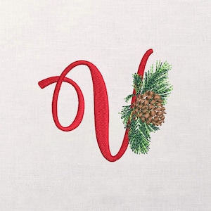 Może przedstawiać: Haftowana czerwona litera "V" z szyszką i gałązkami iglastymi. Litera jest w skrypcie kursywnym, a szyszka jest brązowa z zielonymi igłami. Tło to biała, teksturowana tkanina.