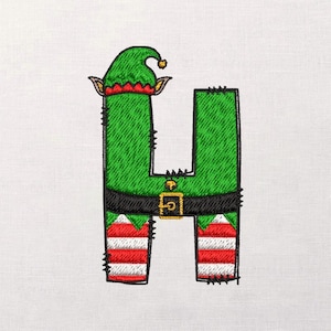 May include: Embroidered letter "H" in an elf costume. The green letter features a matching hat with a gold bell, a black belt with a gold buckle, and red and white striped legs. The background is white.
