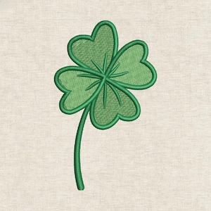 May include: A green four-leaf clover embroidery design. The clover has four heart-shaped leaves with detailed stitching and a stem. The design is on a light beige fabric background.