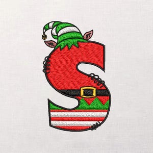 May include: Embroidered letter "S" in a Christmas elf costume. The letter is red with a black belt and gold buckle. The elf hat is green and white striped. The bottom of the letter has green, white, and red stripes.