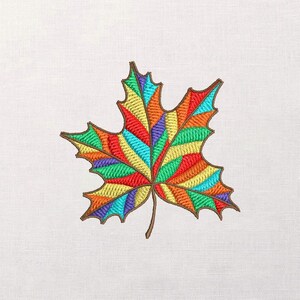 Puede incluir: Hoja de arce bordada en colores vibrantes: rojo, naranja, amarillo, verde y azul. La hoja tiene un contorno y tallo marrón, sobre un fondo blanco. Ideal para manualidades y decoraciones con temática otoñal.