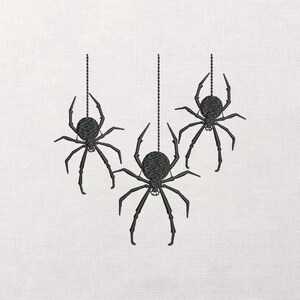 May include: Three black embroidered spiders hanging from strings against a white background. The spiders have detailed legs and bodies, perfect for Halloween or spooky decor.