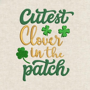 Puede incluir: Diseño bordado con el texto "Cutest Clover in the patch" en hilo verde y dorado. Se incluyen tres tréboles verdes en el diseño. El fondo es de tela beige claro.