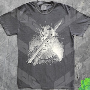 Puede incluir: Una camiseta gris oscuro con un estampado blanco de una persona con una corona y sosteniendo una espada.
