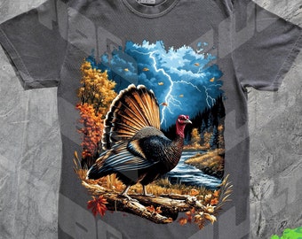 Puede incluir: Una camiseta gris oscuro con un estampado gráfico colorido de un pavo salvaje de pie en una rama en un entorno de bosque. El pavo tiene la cabeza roja y el cuerpo marrón y negro con una cola azul y verde. El fondo presenta un cielo tormentoso con rayos y follaje de otoño.