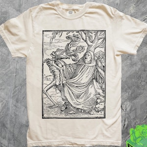 May include: A white t-shirt with a black and white illustration of a figure in a robe holding a scythe and standing next to a tree. The illustration is framed in a black rectangle.