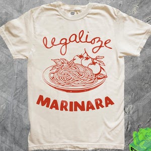 May include: A white t-shirt with the text "legalize marinara" printed in red. The design features a plate of spaghetti with tomato slices.