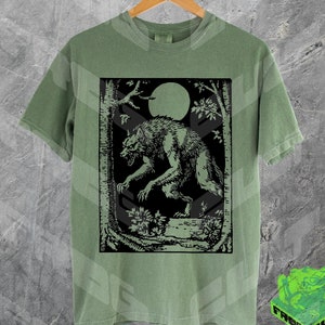 May include: A green t-shirt with a black and white illustration of a werewolf in a forest setting. The werewolf is howling at the moon.