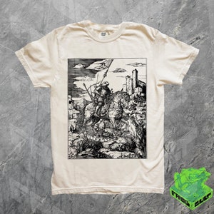 Puede incluir: Una camiseta de color crema con una ilustración en blanco y negro de un caballero a caballo matando a un dragón. La ilustración es de estilo vintage y presenta un castillo en el fondo.