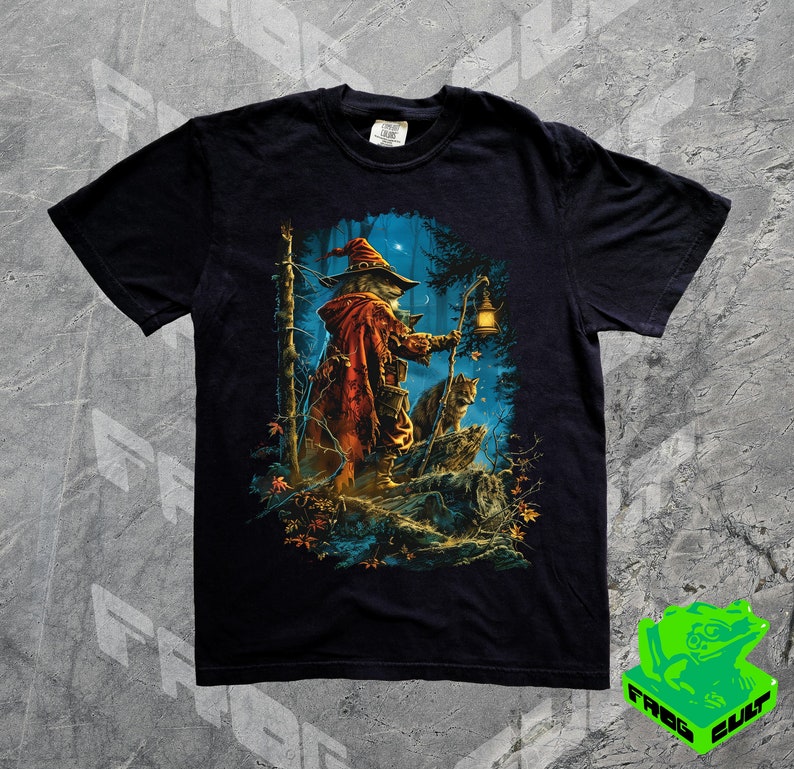 Puede incluir: Camiseta negra con un estampado gr&aacute;fico de un mago con un gato en un entorno de bosque. El mago lleva una t&uacute;nica roja y un sombrero puntiagudo. El gato est&aacute; sentado en una roca. El fondo es un bosque oscuro con &aacute;rboles y estrellas.