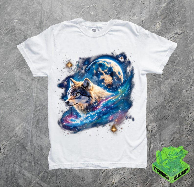 Puede incluir: Camiseta blanca con un gr&aacute;fico de un lobo aullando a la luna en un entorno de galaxia. El lobo es gris y blanco, y la galaxia es azul, p&uacute;rpura y rosa.