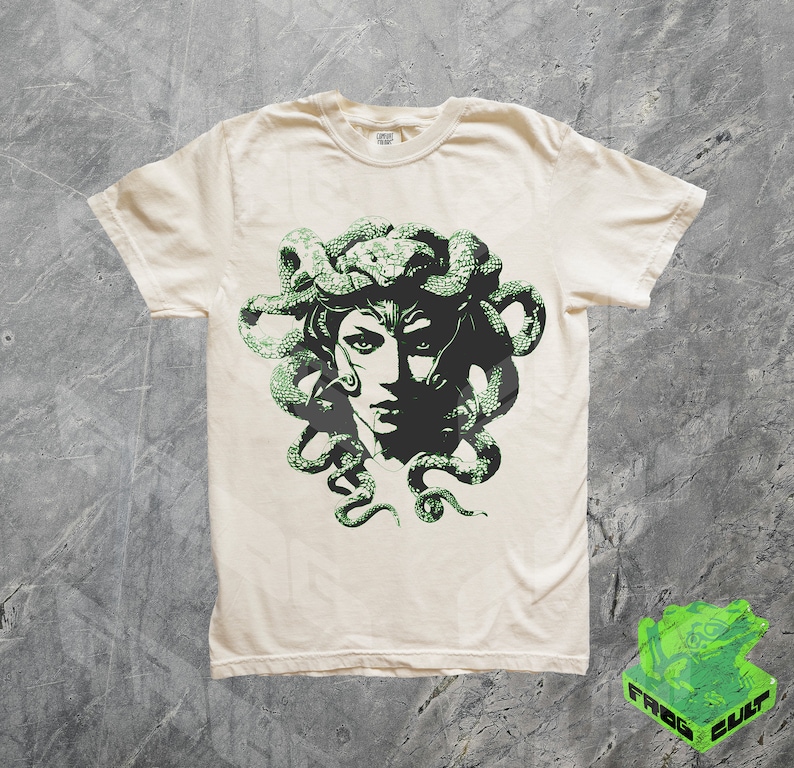 May include: A white t-shirt featuring a green graphic print of Medusa, a mythical Greek figure with snakes for hair.