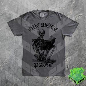 May include: Gray t-shirt featuring a black illustration of a skeleton reading a book. The text "ONEMORE" is above the skeleton, and "PAGE" is below. The shirt has a crew neck and short sleeves.