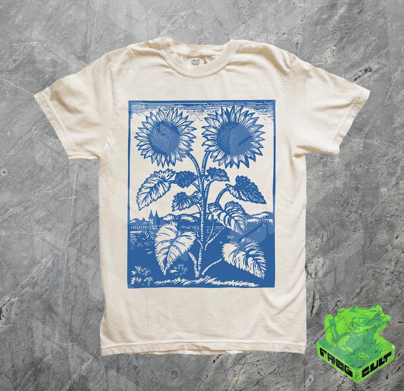May include: A white t-shirt with a blue print of two sunflowers. The sunflowers are stylized and have a vintage look.