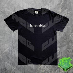Może przedstawiać: Czarny T-shirt z nadrukiem "i have rabies" w kolorze białym na przodzie. Koszulka ma wyblakły, vintage'owy wygląd.