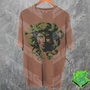 May include: A brown t-shirt featuring a green and black graphic print of Medusa, a mythical Greek figure with snakes for hair.