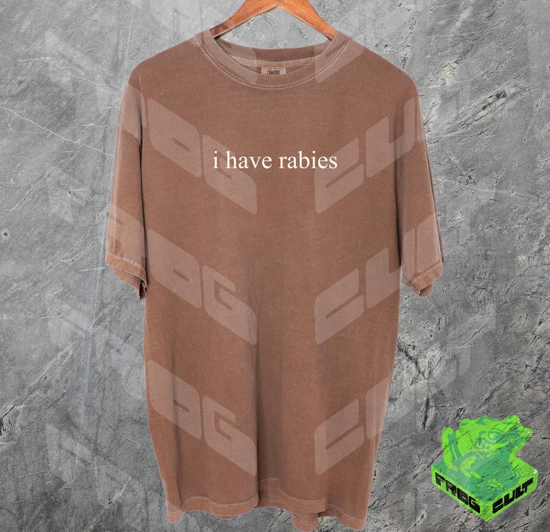 Może przedstawiać: Brązowy t-shirt z nadrukiem "i have rabies" w kolorze białym na przodzie.