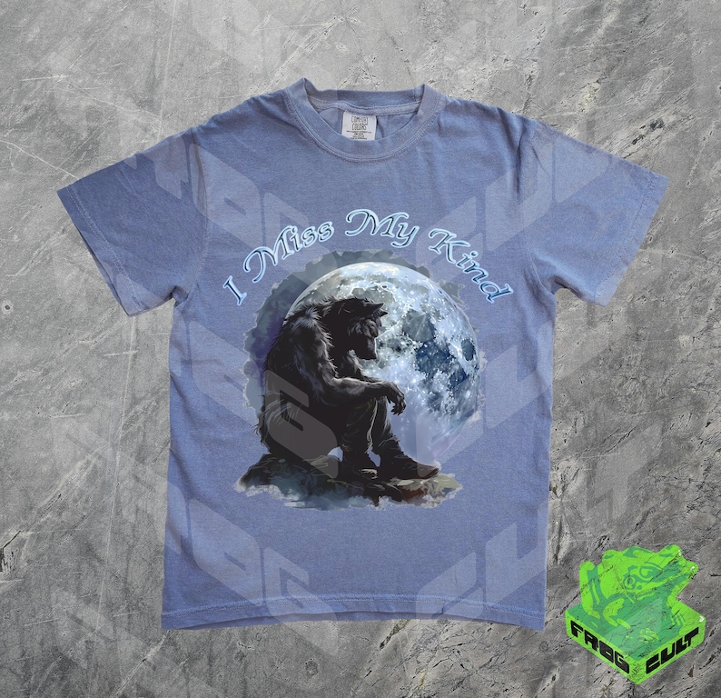 May include: A light blue t-shirt with a graphic of a werewolf sitting under a full moon. The text "I Miss My Kind" is printed on the shirt.