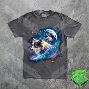 Puede incluir: Una camiseta gris con un lobo aullando a la luna en un estampado de galaxia. El lobo es blanco y gris con una galaxia azul detr&aacute;s. La luna es de color azul claro.