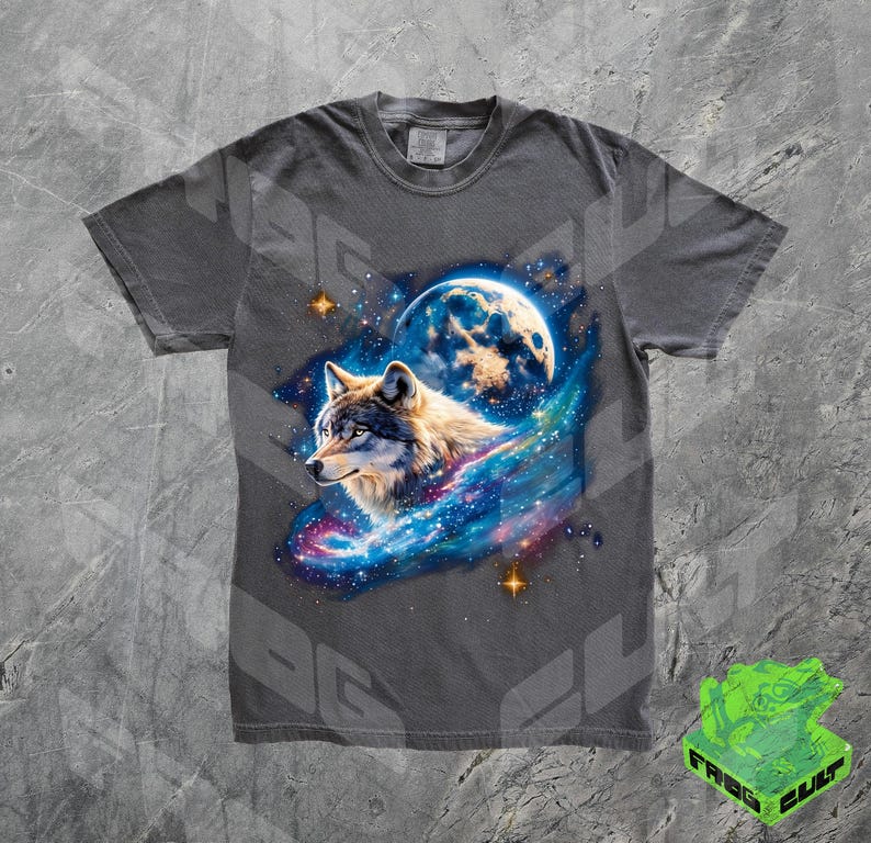 Puede incluir: Una camiseta gris con un lobo aullando a la luna en un estampado de galaxia. El lobo es blanco y gris con una galaxia azul detr&aacute;s. La luna es de color azul claro.