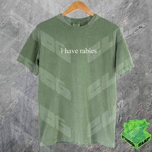 Może przedstawiać: Zielony T-shirt z nadrukiem "i have rabies" z przodu.