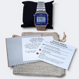 May include: A retro-style digital watch with a blue face and silver band, displayed on a black pillow. The watch face shows the time. Included are care instructions and a cleaning cloth.
