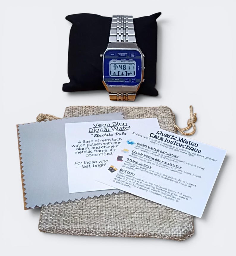 May include: A retro-style digital watch with a blue face and silver band, displayed on a black pillow. The watch face shows the time. Included are care instructions and a cleaning cloth.