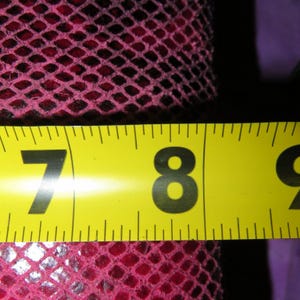 Peut inclure: Gros plan d'un ruban &agrave; mesurer jaune affichant les chiffres 7 et 8 en noir. Le ruban mesure un tissu rose fonc&eacute; &agrave; motifs de losanges. Le tissu a l'apparence d'un filet.