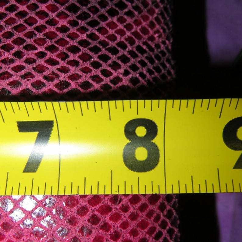 Peut inclure: Gros plan d'un ruban &agrave; mesurer jaune affichant les chiffres 7 et 8 en noir. Le ruban mesure un tissu rose fonc&eacute; &agrave; motifs de losanges. Le tissu a l'apparence d'un filet.