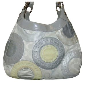 May include: A Coach hobo bag in a light gray and silver color scheme. The bag features a pattern of large, embossed circles with the Coach logo. The top and straps are a solid gray, and the hardware is silver.