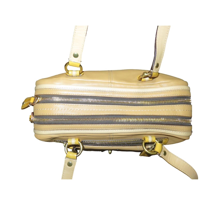 Op de afbeelding: Een bruine leren handtas met twee bovenste handvatten en een ritssluiting. De tas heeft een gele bies en gouden hardware.