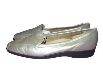 Puede incluir: Un par de mocasines de cuero dorado con punta redondeada y suela negra. Los zapatos sin cordones son probablemente para uso casual. Miden aproximadamente 25 cm de largo.
