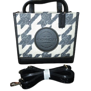 May include: A small, square handbag with a black and white houndstooth pattern. The bag has a black leather base, handles, and trim. A round, textured leather patch with the brand name is centered on the front. Includes a detachable black shoulder strap.