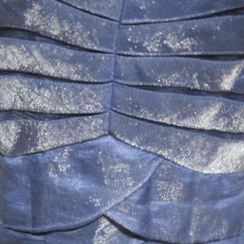 May include: Close-up of a navy blue fabric with a layered design. The fabric has a shimmering, glittery texture, with horizontal folds creating a textured pattern. The folds are slightly curved, adding depth to the design.