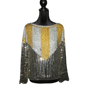 May include: A sequined top with a striped pattern in gold and silver. The top has long sleeves and a round neckline.