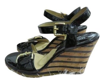 Könnte beinhalten: Schwarze Keilsandalen aus Lackleder mit goldfarbenen Schnallen. Der Keilabsatz hat ein gestreiftes Muster in Braun- und Beigetönen. Die Sandalen haben einen Knöchelriemen und einen Zehenriemen.