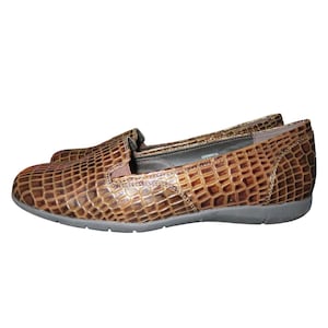 Puede incluir: Zapatos de piel marrón de vestir con un patrón de cocodrilo. Los zapatos tienen una suela plana y una punta puntiaguda.
