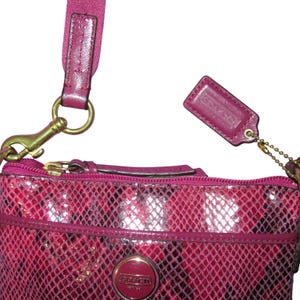 Peut inclure: Un sac bandouli&egrave;re Coach rose avec un motif peau de serpent. Le sac a une fermeture &eacute;clair dor&eacute;e, une sangle rose assortie et une petite &eacute;tiquette en cuir. Le logo Coach est visible &agrave; l'avant du sac.