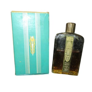 Puede incluir: Un frasco de agua de tocador vintage de vidrio en una caja de color turquesa. El frasco tiene una tapa dorada y una etiqueta dorada con el texto "Sweet Inspiration" y "Toilet Water Avon Products Inc."