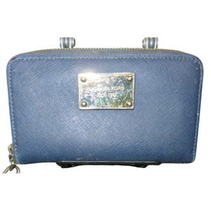 May include: A navy blue wallet with a silver zipper and a silver metal plate that reads "MICHAEL KORS". The wallet has a rectangular shape and a zipper closure. The wallet is made of a textured material.
