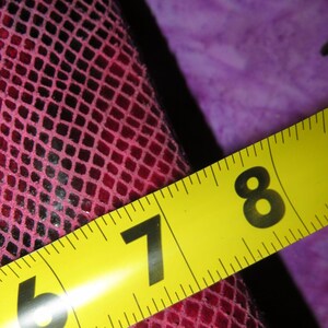 Peut inclure: Gros plan sur un mat&eacute;riau &agrave; motifs rose et noir avec un ruban &agrave; mesurer jaune. Le ruban indique des mesures de 17,78 et 20,32 cm. Le mat&eacute;riau pr&eacute;sente un motif en forme de grille.