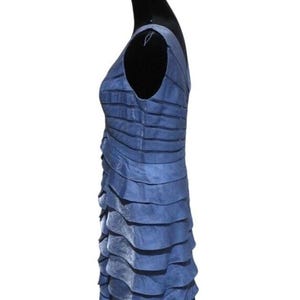 May include: A sleeveless, knee-length blue dress with a layered, ruffled design. The dress is made of a shiny fabric and has a V-neckline. The dress is displayed on a black mannequin.