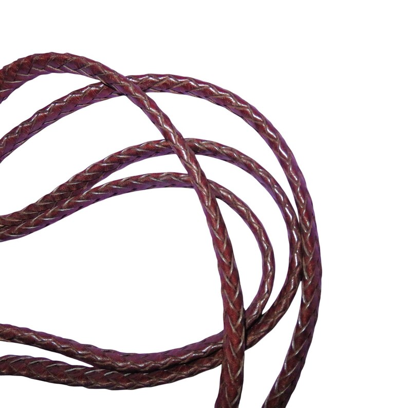 May include: Close-up of a braided leather cord in a deep burgundy color. The cord is tightly woven with a visible pattern and a lighter, silver-toned thread running through the braid. The cord is looped and curved against a white background.