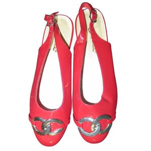 May include: Pair of red patent leather slingback flats. The shoes have a silver-tone chain detail across the toe and adjustable ankle straps. The flats are a vibrant red color and appear to be unworn.