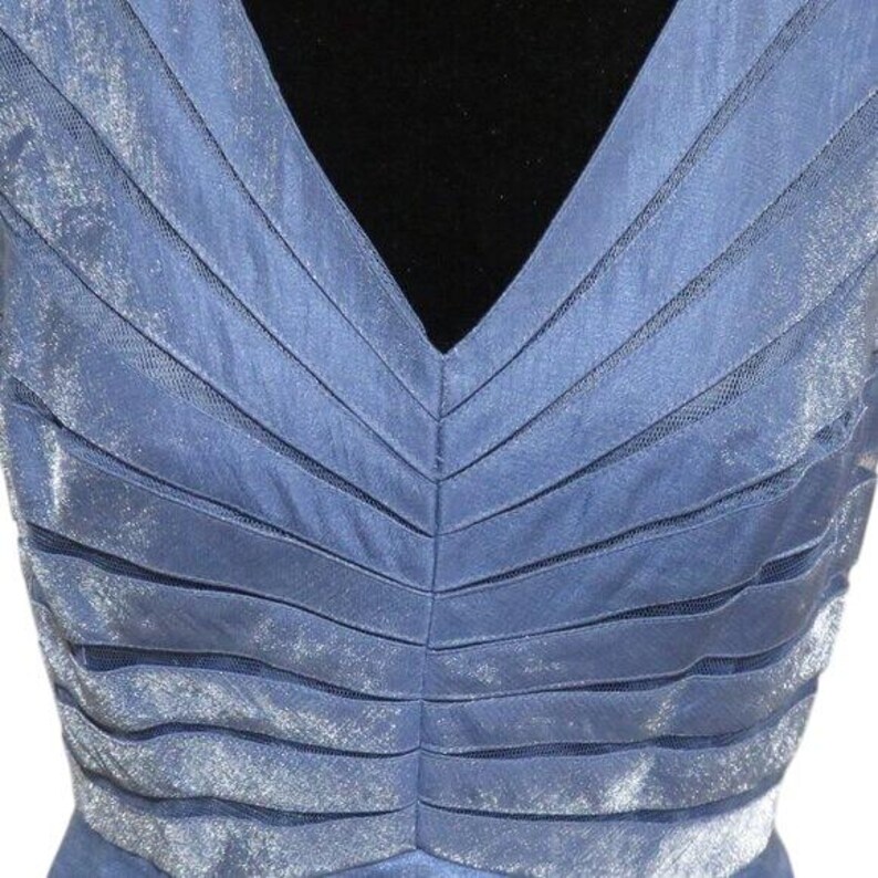 May include: A sleeveless, periwinkle blue dress with a V-neckline. The bodice features horizontal, layered fabric panels with a sheer mesh overlay. The dress has a shimmering, iridescent quality.