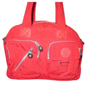 May include: A red nylon handbag with two zippered front pockets and a small pocket with a flap. The bag has two top handles and a shoulder strap. The brand logo is visible on the front.