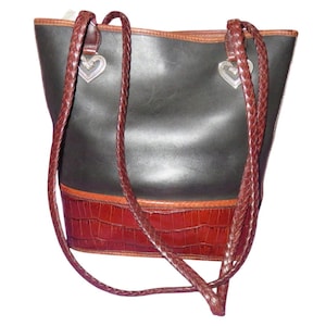 May include: Black leather tote bag with brown braided straps and a brown faux crocodile bottom. The bag has silver heart-shaped charms and a brown trim.