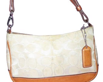 May include: Cream-coloured shoulder bag with a repeating pattern. The bag has brown leather trim at the base and sides, with a matching leather strap. A small leather tag hangs from a chain attached to the bag.